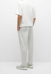 Pantaloni di cotone grigi chiari con tasche laterali, abbinati a una maglietta bianca dalla vestibilità ampia. Le scarpe presentano un design grigio e bianco.