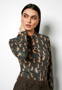 Patterned blouse featuring a dark green background, beige animal print, a button-up front, and long sleeves with buttoned cuffs.