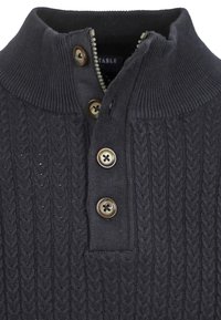 Donkergrijze kabelgebreide trui met geribbelde textuur, voorzien van een korte ritssluiting en vier bruine knopen langs de knopenbies.