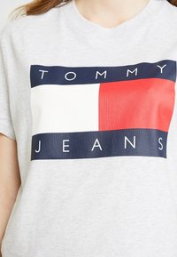 Grå bomullströja med en djärv grafisk logotyp med röda, vita och marinblå sektioner, 'TOMMY' och 'JEANS' i versaler.