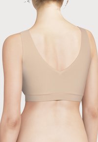Beige, sømløs BH med brede stropper og dyp V-ryggdesign. Laget av glatt, elastisk materiale med et minimalistisk utseende.