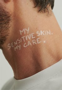 Close-up of skin on the neck with visible texture; white text reads "MY SENSITIVE SKIN. MY CARE." A plain white collar is also visible.