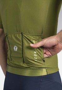 Maillot de cyclisme vert olive à manches courtes, avec une poche zippée à l'arrière, un ourlet élastique et des accents noirs pour plus de détails.