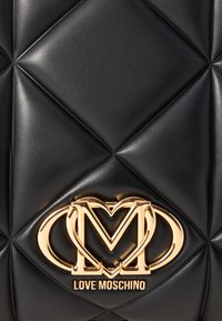 Melns izšūtu sintētisko somu ar spīdīgu apdari, kas aprīkota ar zelta metāla logotipu un uzrakstu "LOVE MOSCHINO" apakšā.