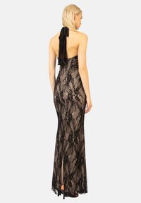 Abito da sera in pizzo nero con collare halter e schiena scoperta. Presenta intricati motivi in pizzo e una silhouette lunga e aderente con uno spacco laterale.