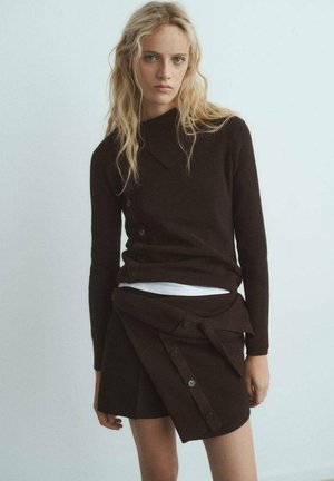 Brown ribbed sweater with a folded collar and button details, paired with a matching wrap skirt featuring buttons and a knot at the waist.