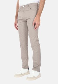 Pantaloni beige in misto cotone con una vestibilità slim, design a cinque tasche e dettagli di cucitura sottili, abbinati a sneakers bianche.