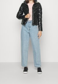 Czarna, błyszcząca kurtka puchowa o krótkim kroju, noszona na jasnoróżowej koszuli. Połączona z jasnoniebieskimi dżinsami o wysokim stanie i czarnymi butami.