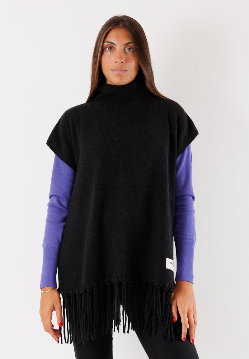 Poncho nero in lana con collo alto, caratterizzato da maniche corte e un bordo frangiato. Sotto, si intravede una maglietta viola a maniche lunghe.