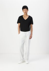 Sort V-hals t-shirt kombineret med lys grå sweatpants. Sweatpantsene har en elastisk talje. Modellen har hvide sneakers på.