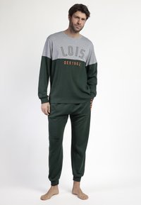 Chándal verde y gris con mangas largas; presenta "LOIS DEN1962" en letras naranjas en el pecho y el costado. Tejido suave y texturizado.