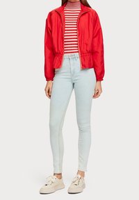 Rød vindjakke med elastisk talje, parret med en stribet turtleneck og lyseblå skinny jeans. Hvide sneakers fuldender outfittet.