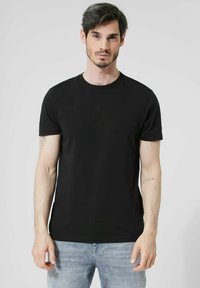 Černé tričko s krátkým rukávem vyrobené z bavlny s kulatým výstřihem. Model ukazuje tetování na levém rameni. Jednobarevné bez vzorů.