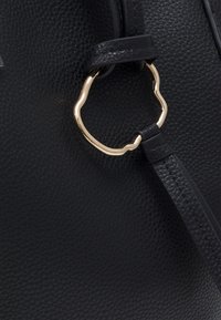 Černá kožená kabelka s texturovaným povrchem, zlatými kovovými doplňky a zakřiveným akcentovým kroužkem s elegantním úchytkou.