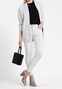 Light gray cardigan over a black t-shirt, white skinny jeans, and snake-print heels. A small black handbag completes the outfit.