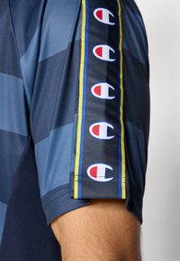 T-shirt de sport à manches courtes en bleu foncé avec des rayures diagonales, arborant un logo coloré sur la manche et des accents contrastés.