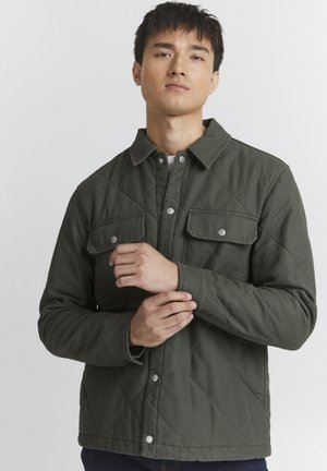 Quilted green jacket with a snap button closure, two chest pockets, and a collared neckline, featuring a textured fabric and diamond pattern.