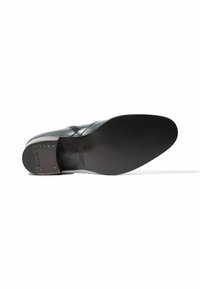 Zapato de cuero negro con un empeine liso, puntera afilada y suela plana. Los detalles notables incluyen costuras y un tacón cuadrado con acentos metálicos.