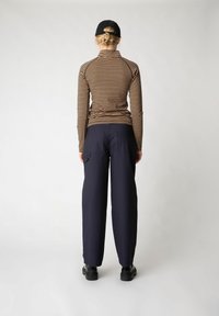 Maglietta a maniche lunghe a righe in marrone e nero, abbinata a pantaloni larghi blu navy. L'outfit presenta un collo alto e tasche pratiche.