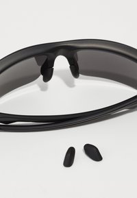Schwarze Sonnenbrille aus Kunststoff mit dunklen Gläsern und geschwungenem Design. Enthält zwei abnehmbare Nasenpolster in Schwarz.