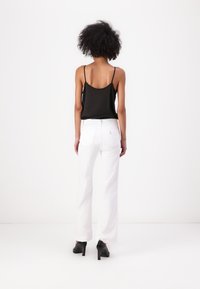 Camisola in satin nero con spalline sottili abbinata a pantaloni bianchi a gamba larga, con vita alta e tasche posteriori. Indossata con tacchi neri.