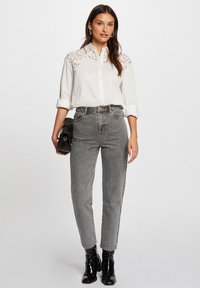 Camicia bianca con bottoni e dettagli in pizzo sulle spalle, abbinata a jeans grigi a vita alta. Stivali neri alla caviglia e una piccola borsa nera.