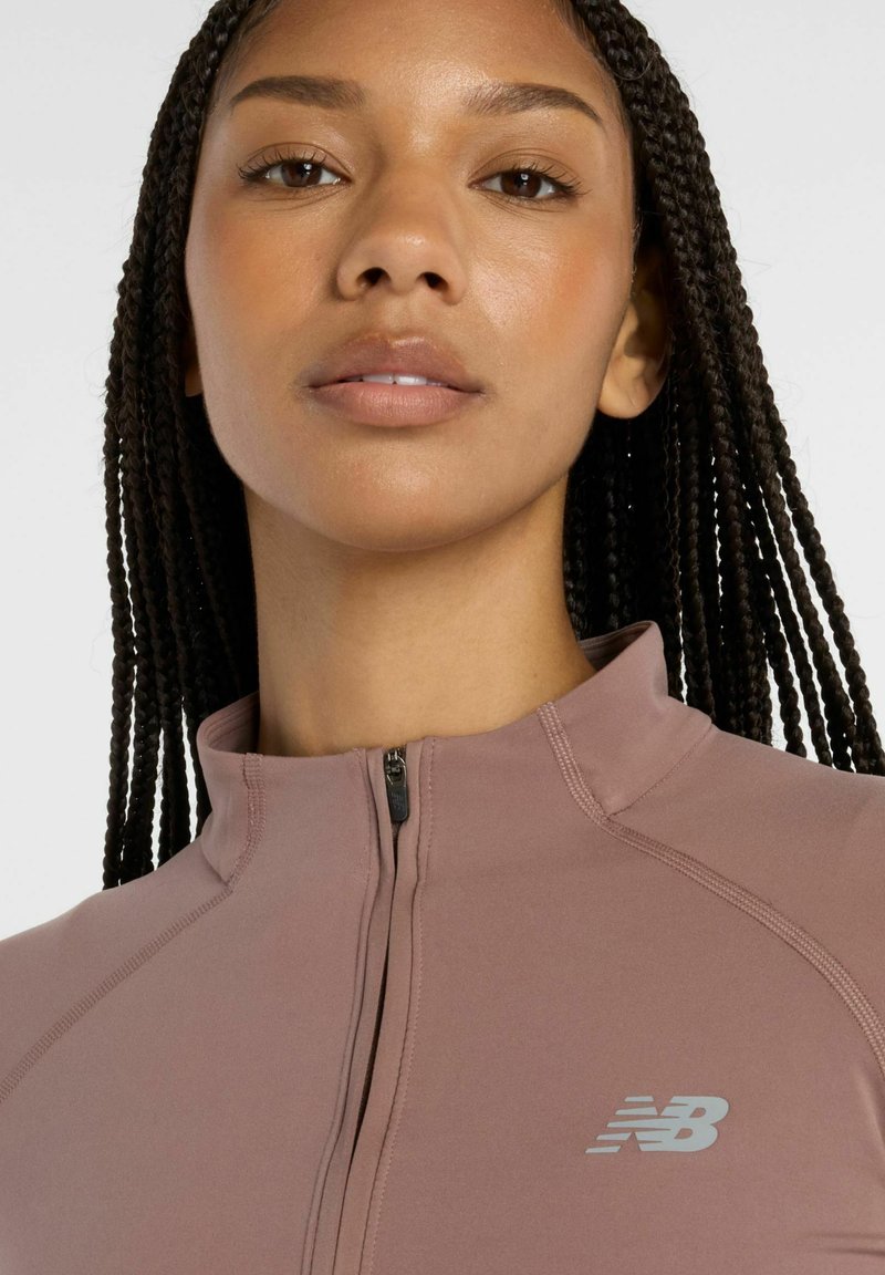 Chaqueta deportiva de color púrpura claro con cuello con cremallera, diseño ajustado y marca visible en el pecho. Textura suave y sin patrones visibles.