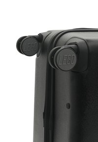 Svart hårdskalväska med slät yta, utrustad med två roterande hjul och en dragkedja; hjulen har ett cirkulärt LEGO-logotyp prägling.