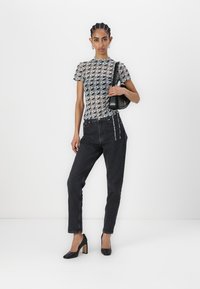 Sheer patterned top in gray with black accents, paired with high-waisted black jeans and black heels featuring a block heel design. Small black handbag.