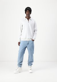 Grijze zip-up sweatshirt, lichtblauwe jeans en witte sneakers, gedragen met een zwarte beanie. Casual pasvorm, minimalistisch ontwerp, zachte stoftextuur.