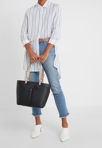 Musta nahkainen laukkumalli, jossa on tekstuuri, beige hihnat ja jämäkkä muotoilu. Yhdistettynä raidalliseen valkoiseen ja siniseen pitkään paitaan, farkkuihin ja avokkaisiin.