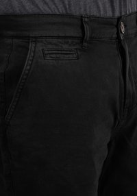 Jean en denim noir avec une coupe classique, design à cinq poches et fermeture à bouton et à zipper visible. Tissu doux avec une légère texture.