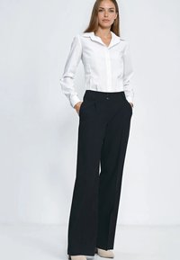 Biała koszula na guziki z ostrym kołnierzykiem, zestawiona z czarnymi spodniami o szerokich nogawkach i beżowymi szpilkami. Gładka tkanina i dopasowany krój.