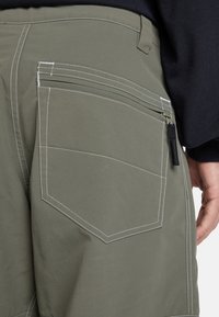 Olive green cargo shorts featuring contrasting white stitching, a side zipper pocket, and a reinforced back pocket design.