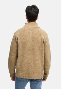 Sweter dziany w kolorze beżowym z wysokim kołnierzem, prążkowanymi mankietami i dołem. Posiada teksturowany, przytulny materiał oraz luźny fason.