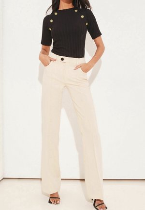 Schwarzes, geripptes Kurzarmoberteil mit goldenen Knöpfen; hoch taillierte, cremefarbene Hose mit weitem Bein, Fronttaschen und schwarzen Knopfakzenten.