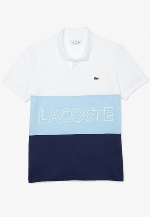 Korte mouwen polo in wit, lichtblauw en marineblauw. Kenmerkt zich door een effen ontwerp met "LACOSTE" in het wit gedrukt over de blauwe streep en een groen logo.