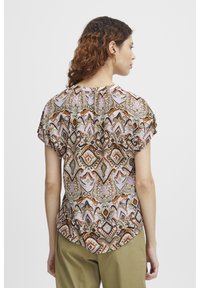 Blouse à motif floral avec des manches courtes, dotée d'un col rond et d'un mélange de teintes marron, rose et verte sur un fond clair.