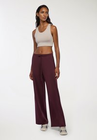 Canotta cropped beige chiaro e pantaloni larghi bordeaux con vita regolabile, abbinati a sneakers grigie e bianche. Tessuto dalla superficie liscia.