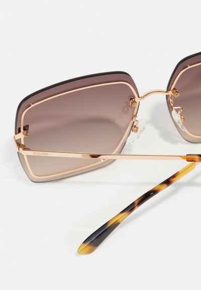 Lunettes de soleil oversize avec verres dégradés marron, monture en métal doré et embouts de branches en écaille de tortue. Équipées de plaquettes de nez ajustables.