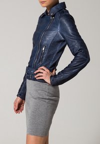 Giacca da motociclista in pelle blu navy con pannelli laterali a coste, chiusura con zip asimmetrica e vita regolabile con cintura. Dettagli testurizzati sulle maniche.