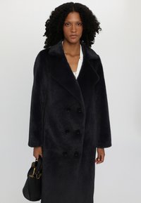Double-breasted dark navy coat made of textured fabric with large black buttons, featuring a notched collar and long sleeves.