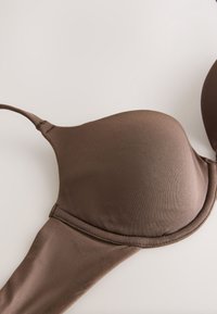 Brun polstret bh med tynde justerbare stropper lagt fladt på en lys overflade, der viser glat stof og syningsdetaljer.