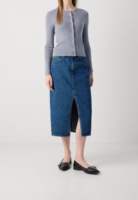 Světlě šedý kardigan se zapínáním na knoflíky, doplněný džínovou midi sukní s předním rozparkem. Celek doplňují černé baleríny s ozdobami.