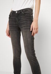 Jeans ajustados de mezclilla negra con una ligera textura desgastada, diseño tradicional de cinco bolsillos y herrajes metálicos en la cintura.