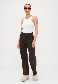 Černé džíny s vysokým pasem, rovný střih, strukturovaný denim, v kombinaci s bílým tílkem a masivními béžovými teniskami, s hnědými slunečními brýlemi.