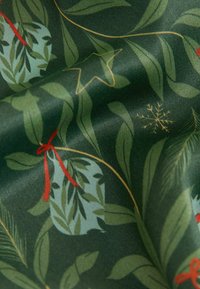 Tissu vert avec un motif de feuilles, agrémenté de rubans rouges et d'accents dorés, ainsi que de feuilles bleu-vert et d'un détail flocon de neige blanc.