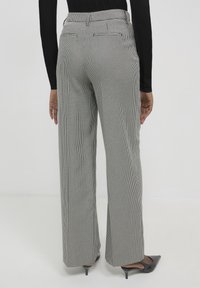 Personne portant un pantalon large à carreaux noir et blanc taille haute, un top noir à manches longues et des kitten heels noires à bout pointu, vu de dos.
