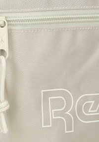 Primer plano de una bolsa de tela beige con una cremallera blanca y texto impreso en blanco que comienza con las letras "Re" en el frente.