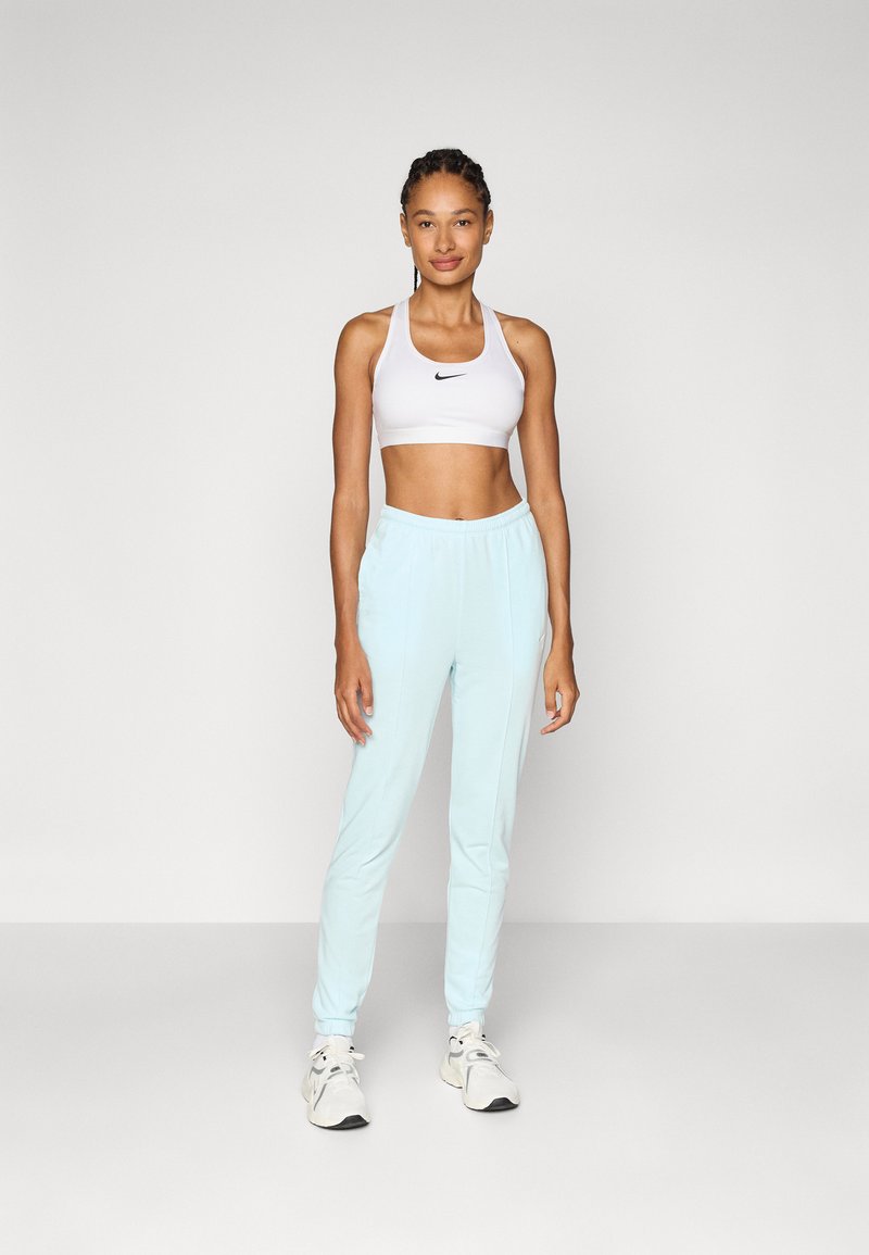 Sujetador deportivo blanco con logotipo negro, joggers azul claro con tapered, banda elástica en la cintura y puños, combinados con zapatillas de deporte grises.